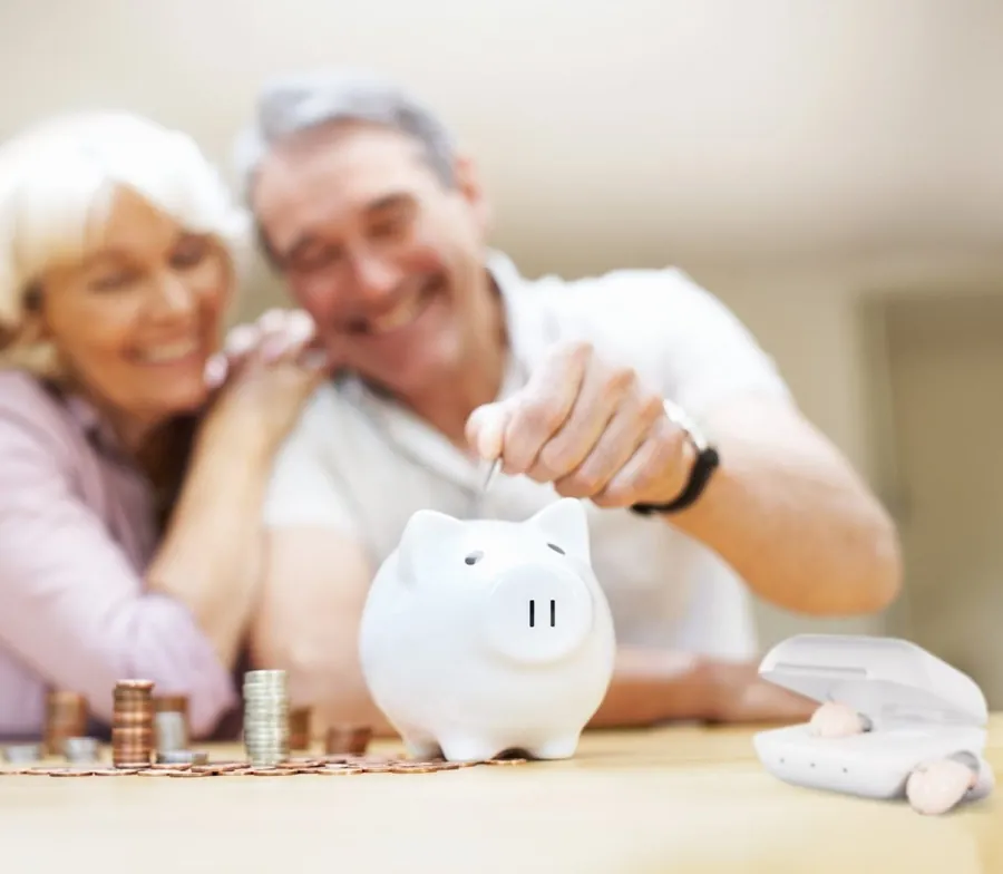 Smiling older couple putting coins into a piggy bank next to a hearing aid charging case