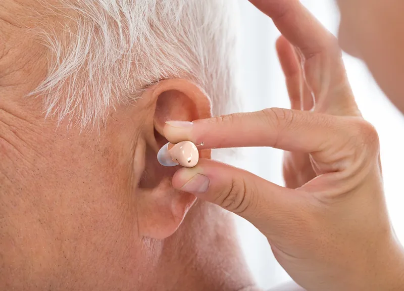 Close-up of a person placing a small hearing aid into their ear